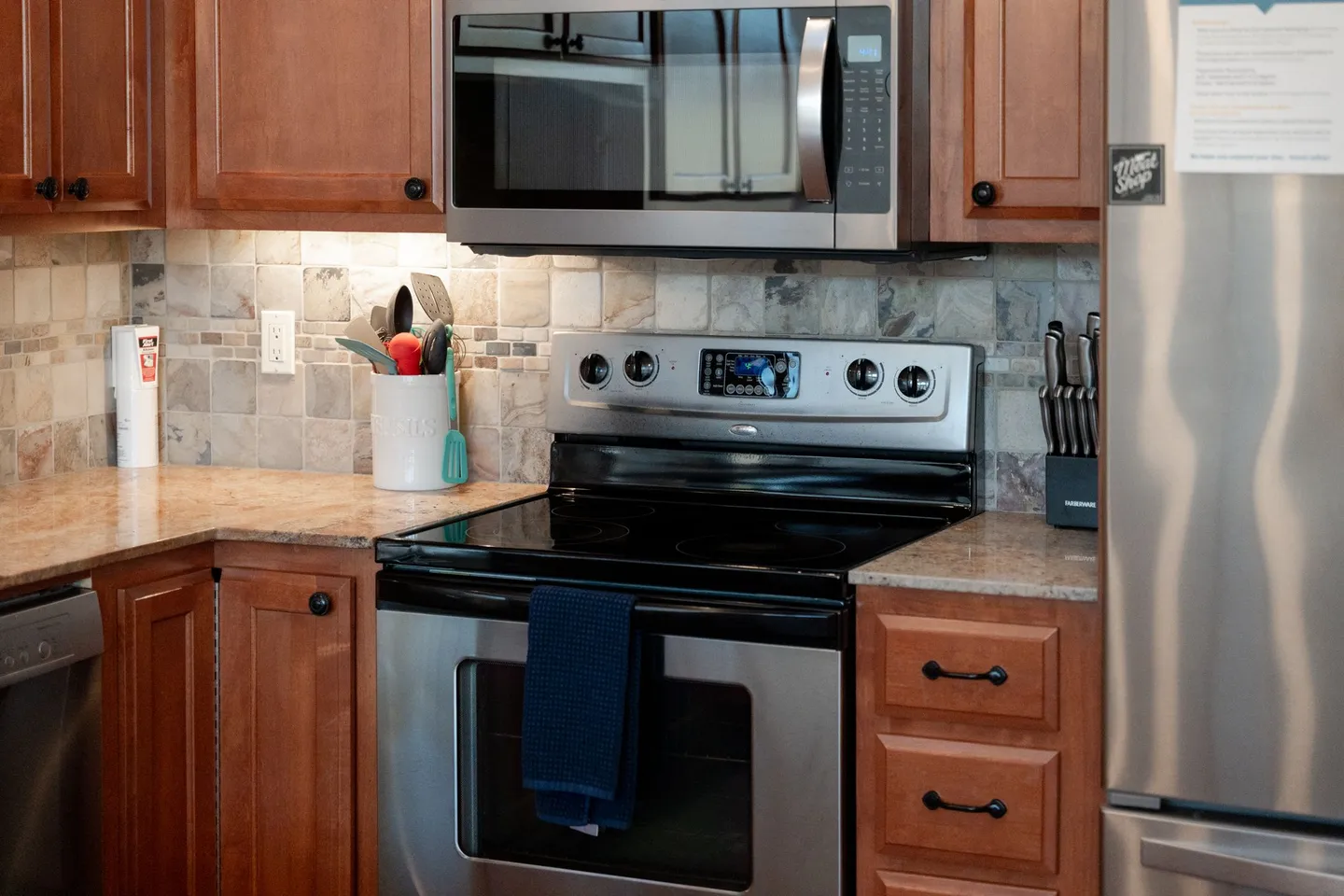Close-up of a kitchen featuring a stainless steel electric range, an over-the-range microwave, wood cabinetry, and a tiled backsplash.