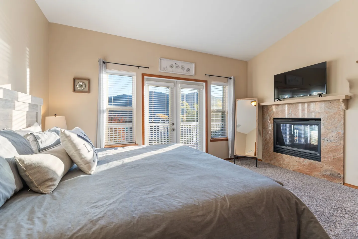 Bedroom featuring a large bed, fireplace with mounted TV above, and glass double doors opening to an outdoor deck.