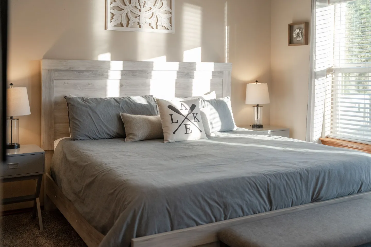 Bedroom with a large bed, light wood headboard, bedside tables with lamps, and sunlight streaming through blinds.