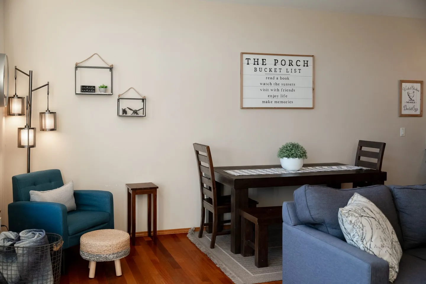 Living and dining space with hardwood floors, a teal armchair, a dark wood dining table, and wall decor.