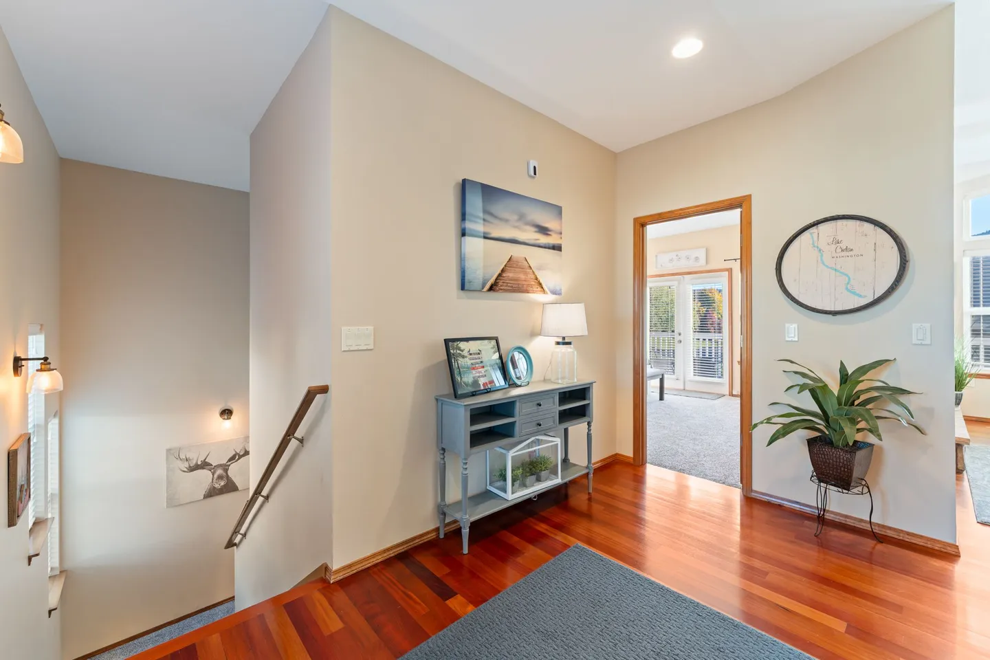 Hallway and entryway with hardwood flooring, a console table with decor, a staircase to the left, and an open doorway leading to a carpeted room.