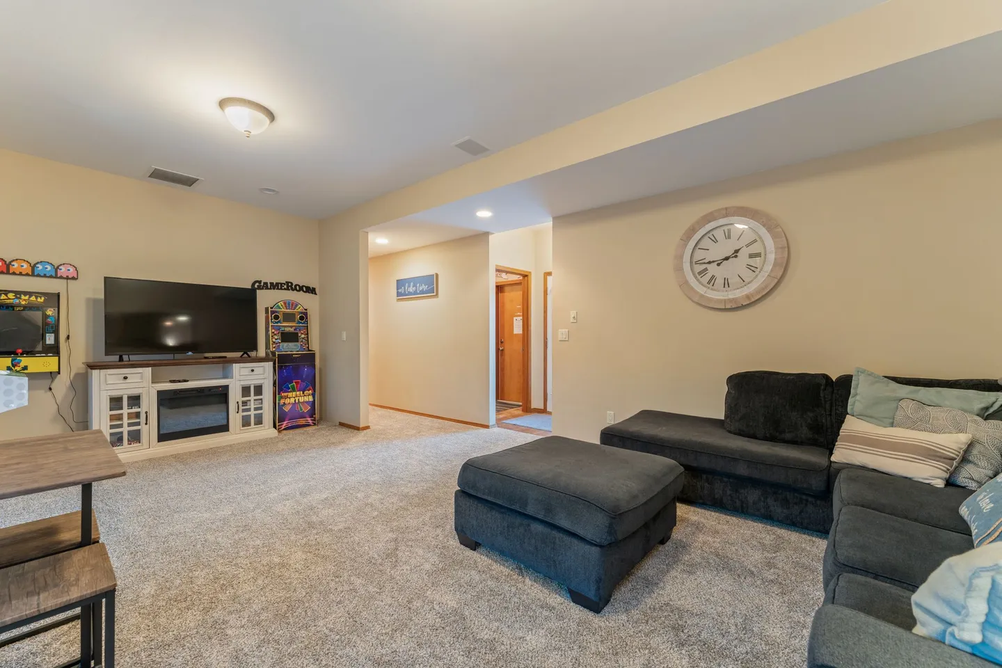 Living room and game area with carpet, a large sectional sofa with an ottoman, a TV on a console, and arcade machines.