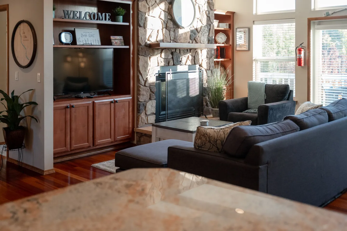 Living room with a stone fireplace, built-in entertainment center, and dark gray sofa.