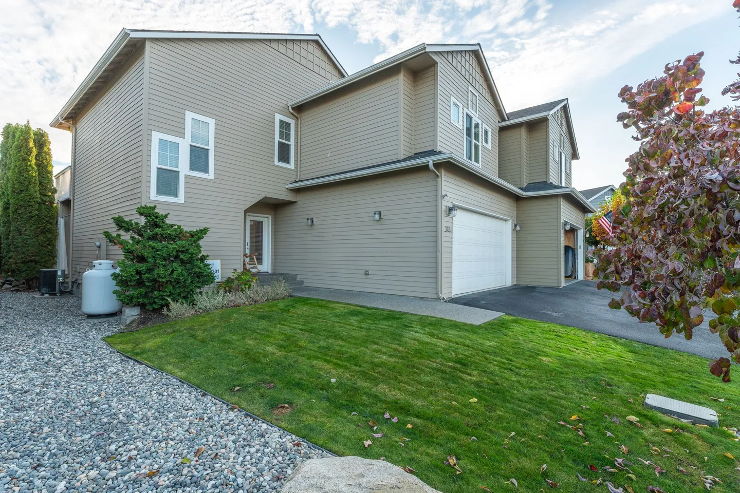 Exterior view of a multi-story home with light brown siding, an attached garage, paved driveway, and grass lawn.