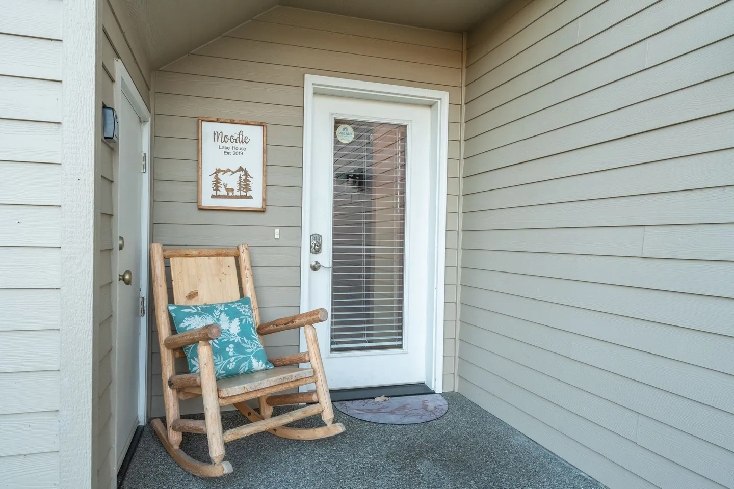 Covered entryway featuring a wooden log rocking chair with a teal cushion next to a white door with glass and internal blinds.