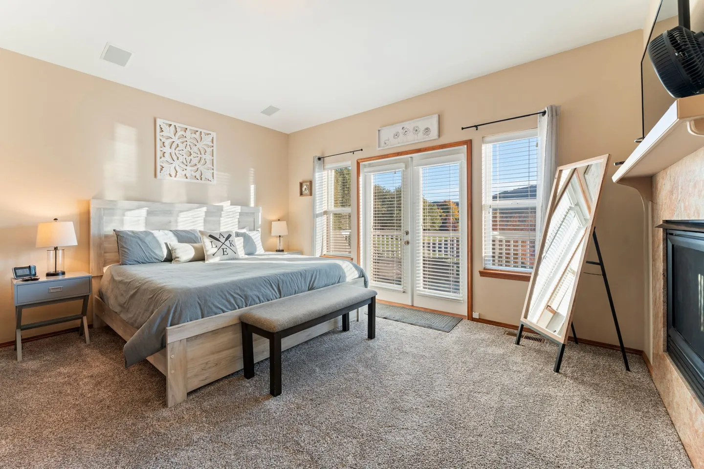 Bedroom with a large bed, bench, full-length mirror, fireplace, and glass doors leading outside.