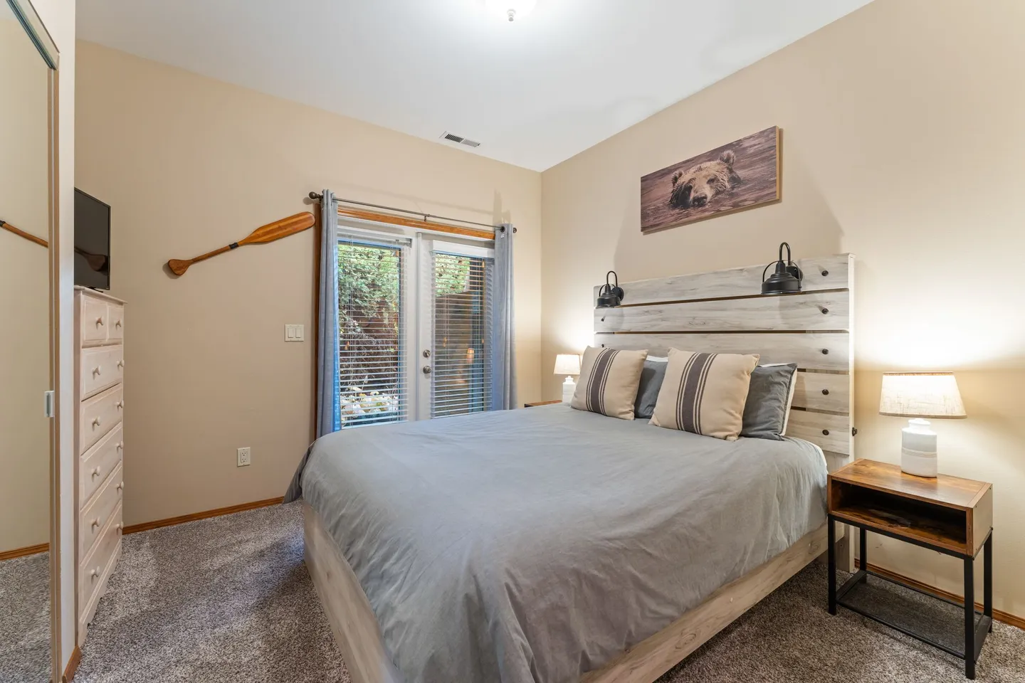 Bedroom with a wooden platform bed, rustic headboard, carpeted floor, and glass French doors leading outside.