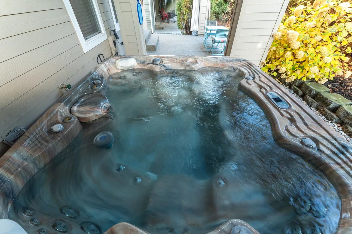 Outdoor hot tub with bubbling water located on a patio next to the house siding.