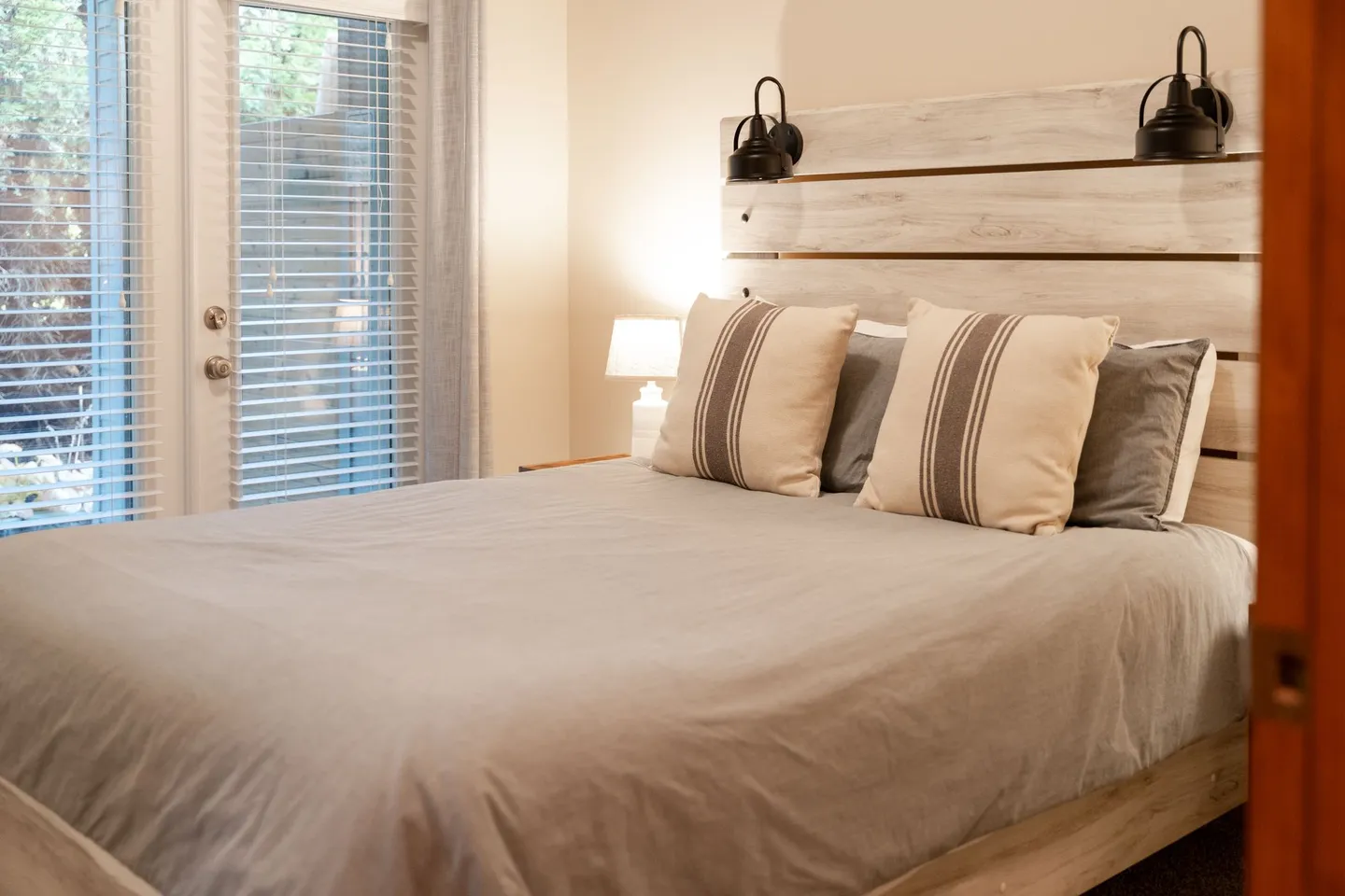 Bedroom featuring a bed with a light wood plank headboard, black mounted reading lamps, and French doors with blinds.