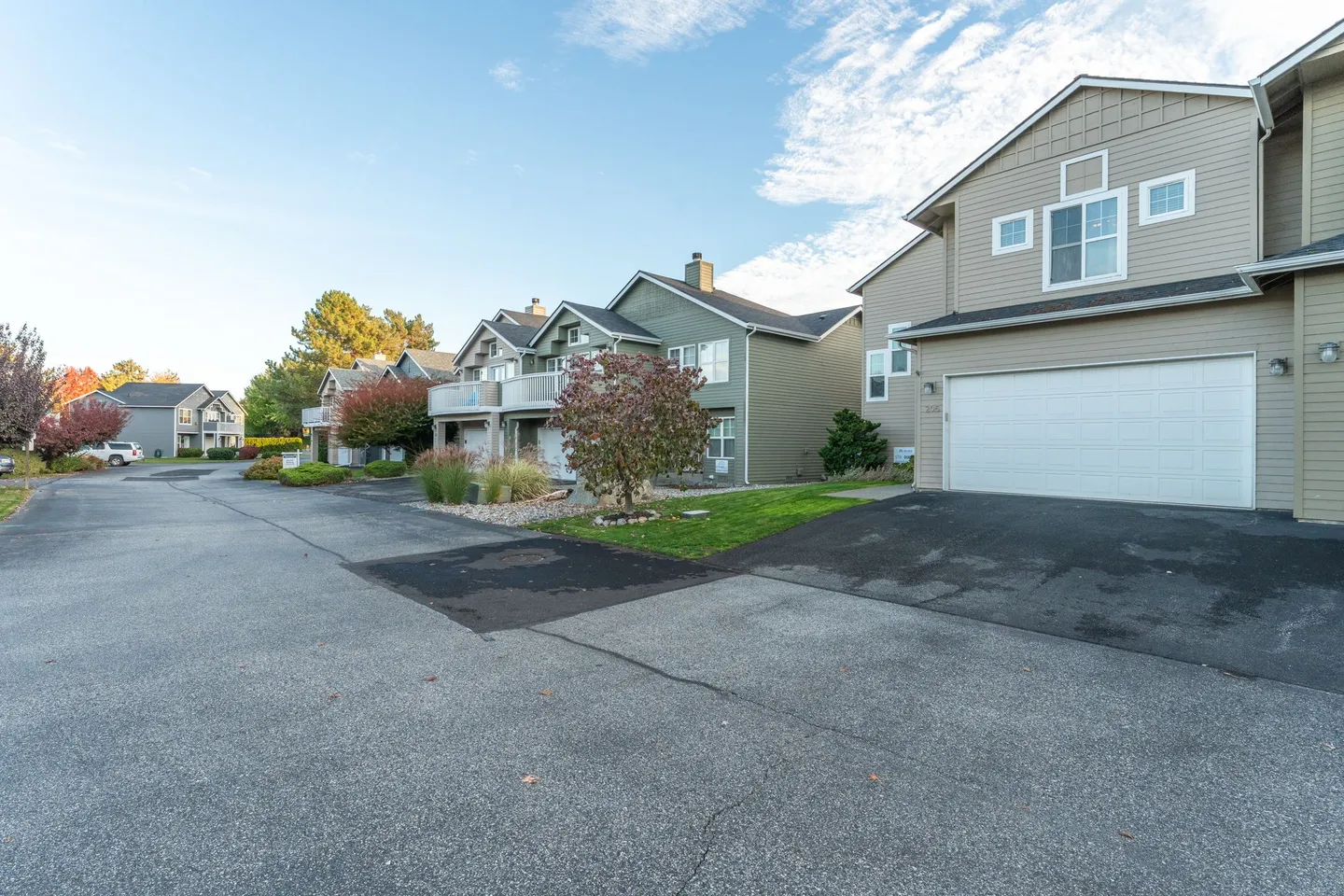 Exterior view of two-story residential townhomes along a paved asphalt driveway under a clear sky.