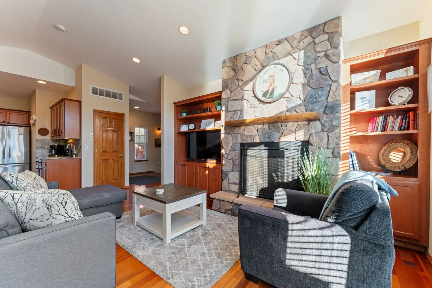 Living room with a stone fireplace, wood shelving, and upholstered seating around a coffee table.