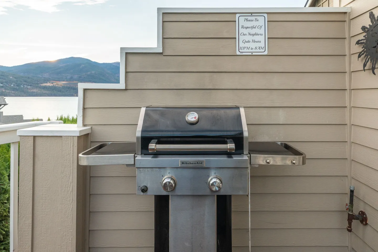 A KitchenAid gas grill situated outdoors against a stepped exterior wall, overlooking a lake and mountains.