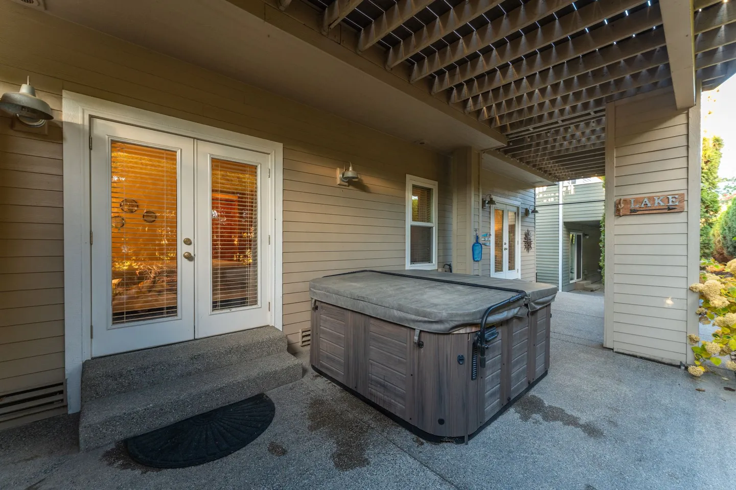 A covered concrete patio with a wood-paneled hot tub and exterior French doors.