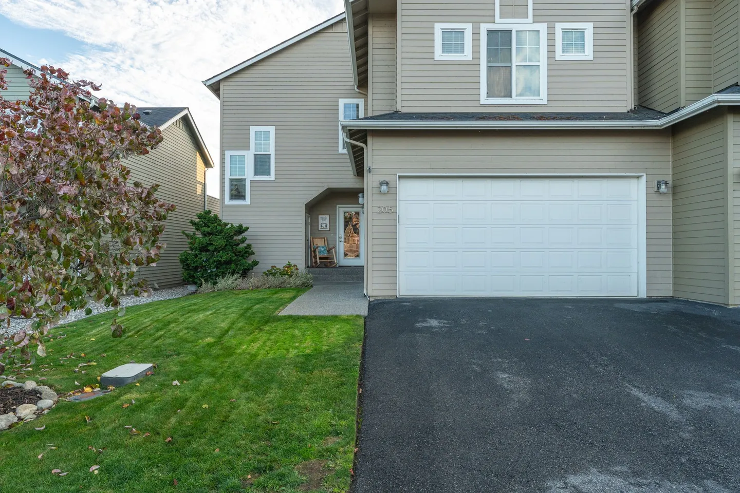 Exterior front view of a two-story home with beige siding, a two-car garage, a paved driveway, and a small front lawn.