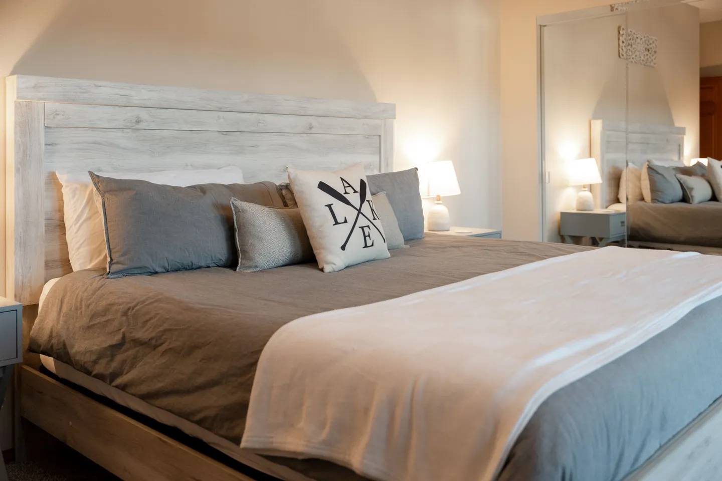Bedroom featuring a made bed with a light wood headboard, gray bedding, decorative lake-themed pillow, and mirrored closet doors.