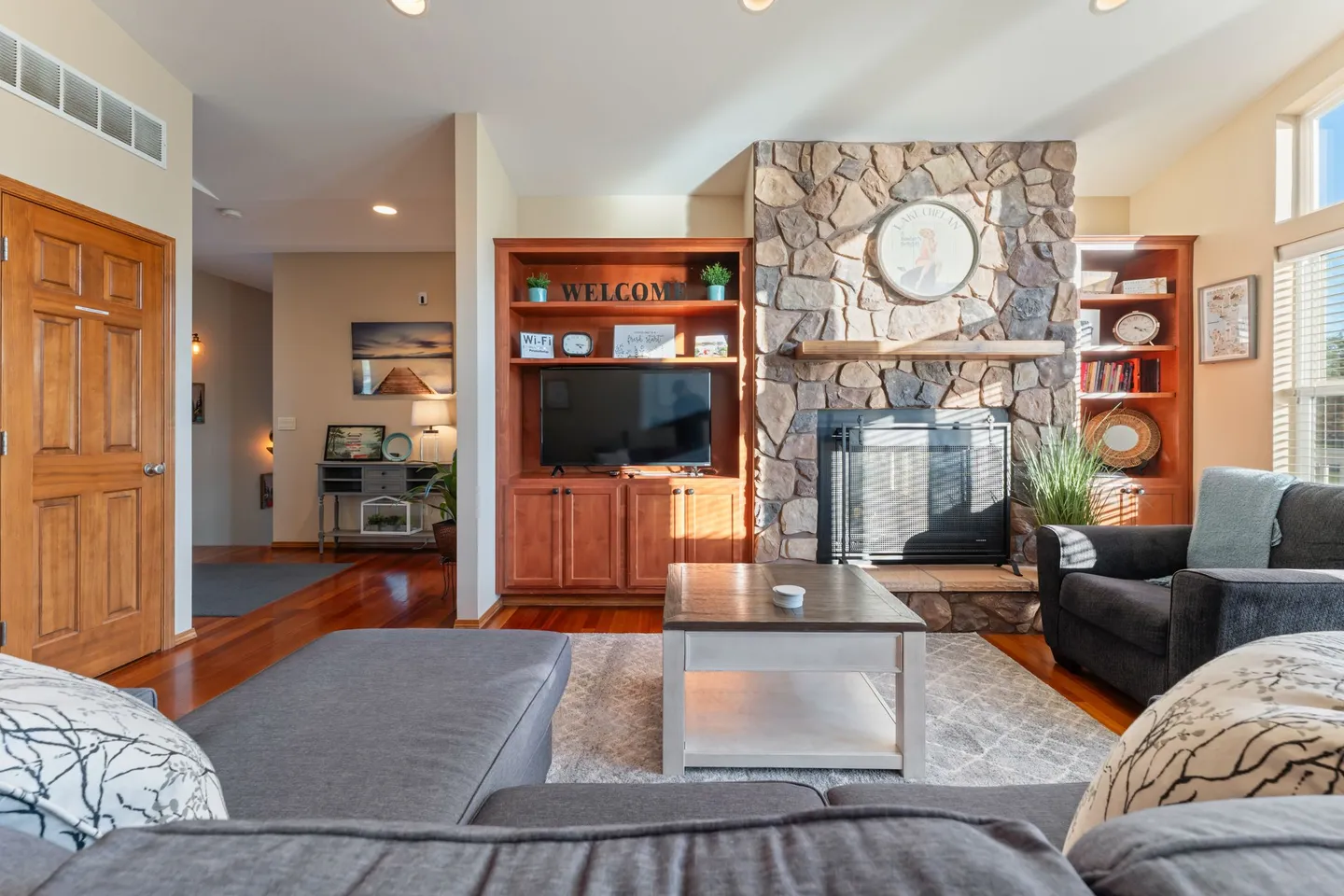 Living room with a stone fireplace, built-in wooden entertainment centers, television, coffee table, and gray sectional sofa.