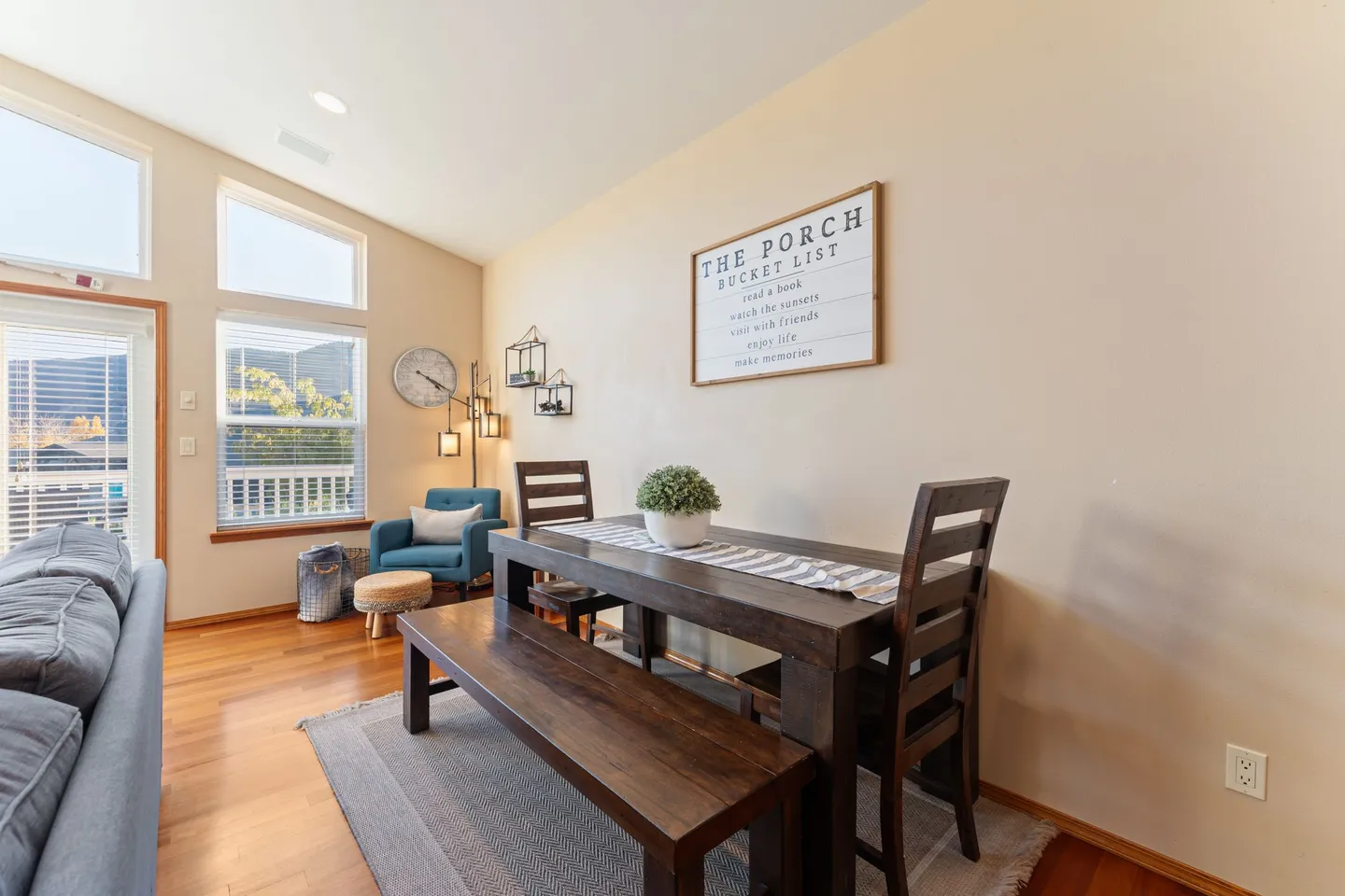 Dining area with a dark wood table, bench, and chairs placed on a small rug beside windows and an armchair in the corner.