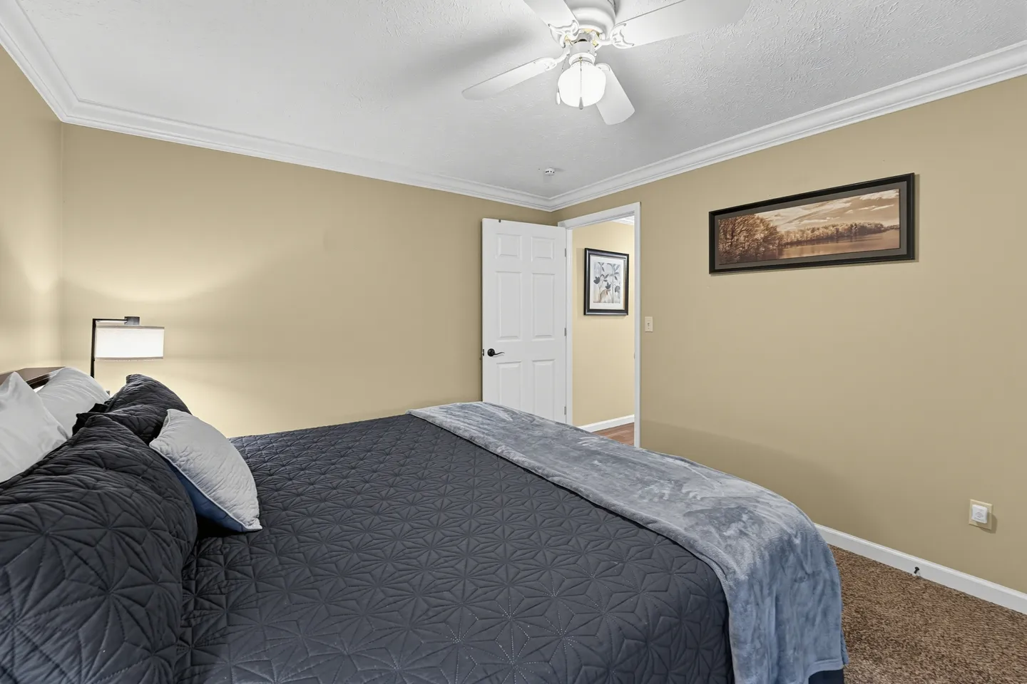 Bedroom featuring a made bed with dark patterned bedding, tan walls, crown molding, and a ceiling fan.