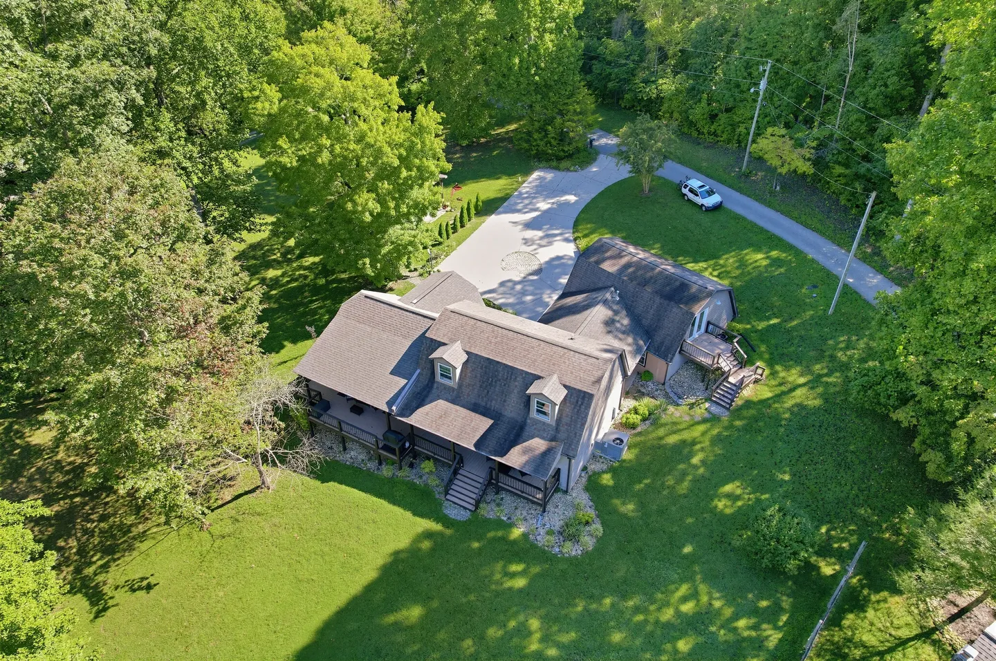 Aerial view of a multi-story home surrounded by dense green trees, a grassy yard, and a curved paved driveway.