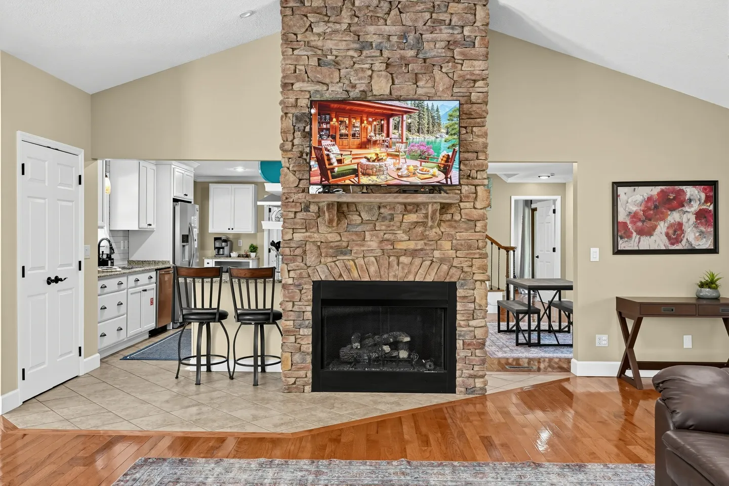 Living area featuring a stone fireplace with a mounted television, flanked by entryways to the kitchen and dining area.