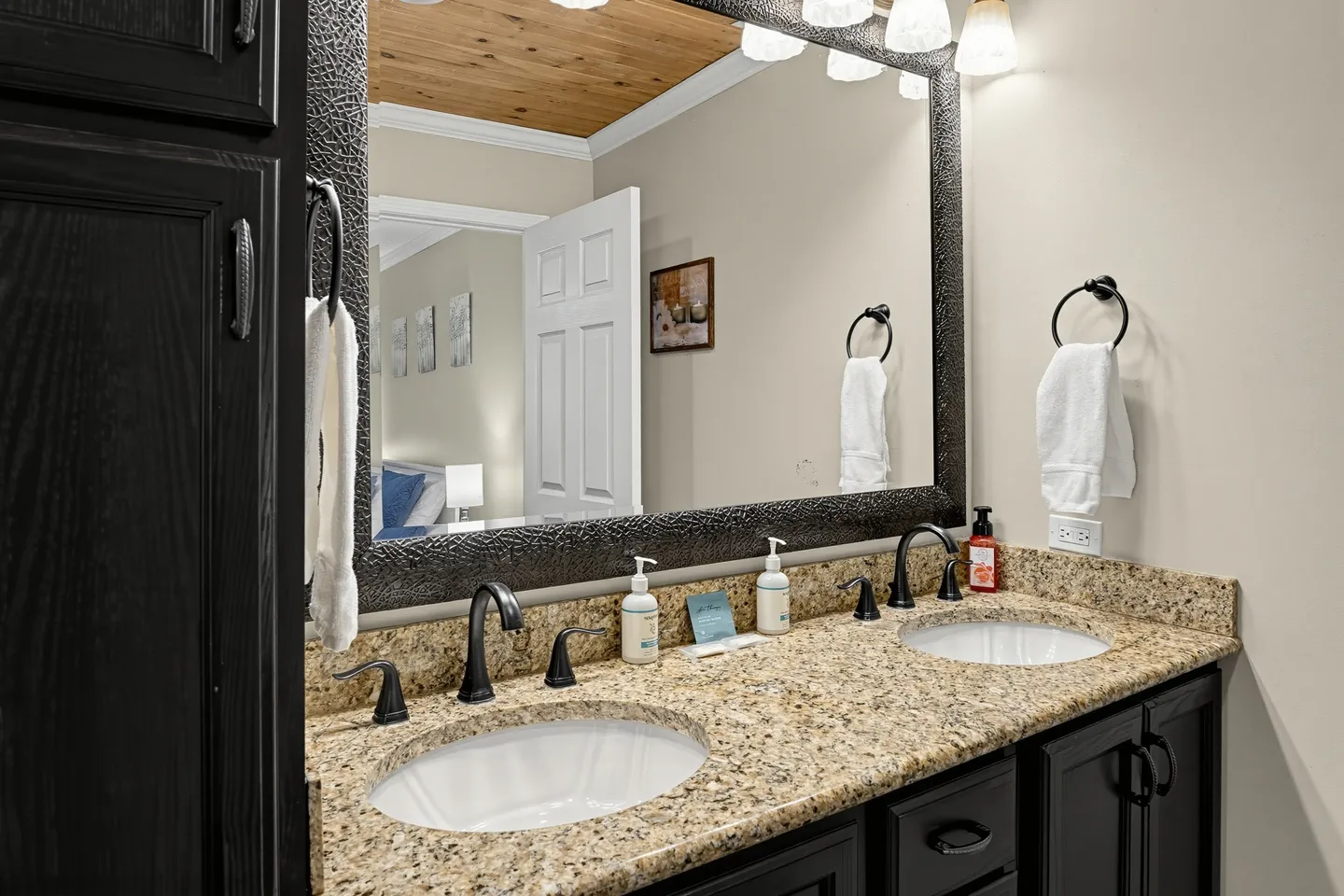 Bathroom vanity with dark cabinets, speckled stone countertop, two undermount sinks, and a large textured mirror.
