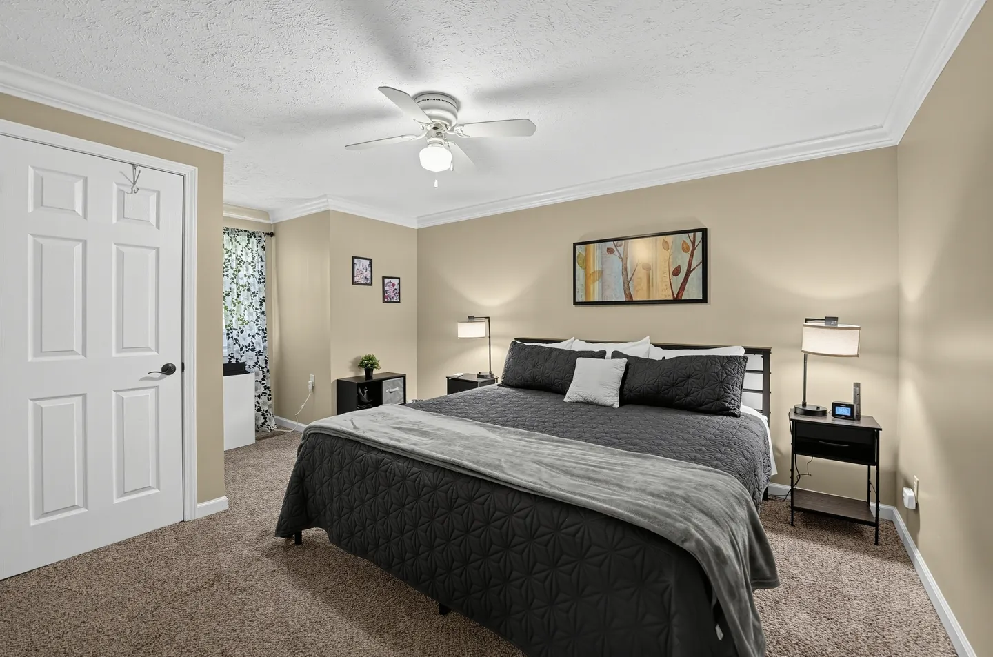 Bedroom with a large bed dressed in dark gray bedding, flanked by nightstands with modern lamps, a ceiling fan, and carpeted floors.