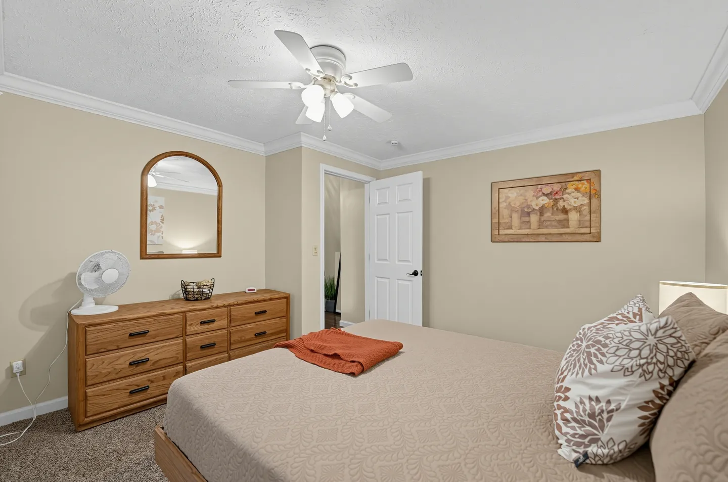 Bedroom featuring a made bed with an orange throw, a wooden dresser with a mirror, and a white ceiling fan.