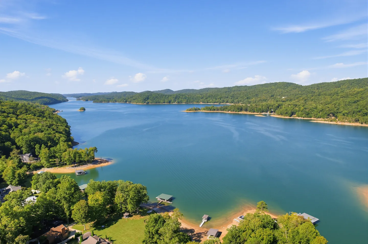 High aerial view of a wide blue lake surrounded by forested rolling hills with boat docks along the shoreline.