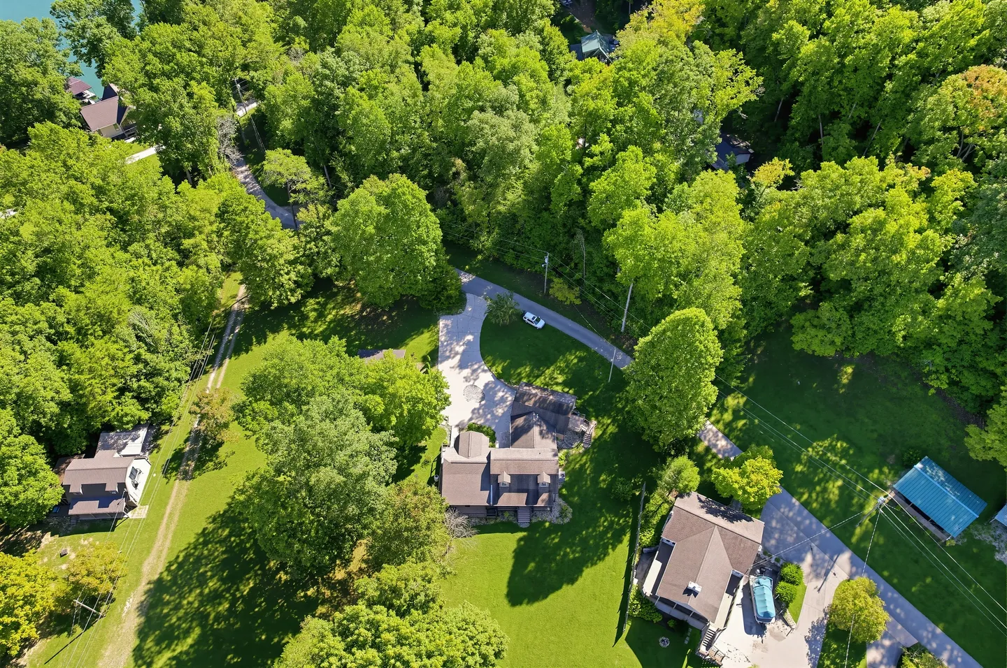 High-angle aerial view of a house nestled in a dense green forest with a paved driveway and neighboring homes.