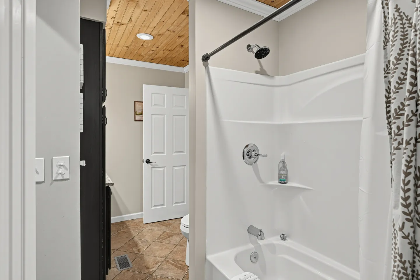 Bathroom with a white bathtub and shower surround, tile flooring, and wood-paneled ceiling.