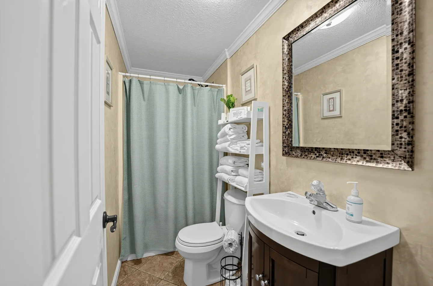 Bathroom featuring a vanity sink, toilet with an over-the-toilet towel shelf, a light green shower curtain, and a mosaic-framed wall mirror.