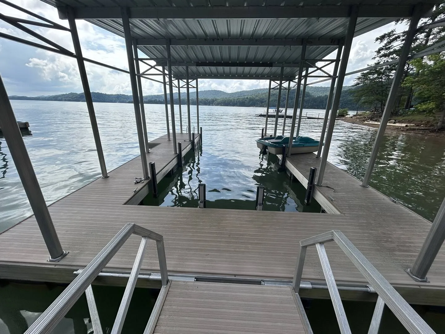 A covered floating boat dock on a lake with boat slips and a paddle boat.