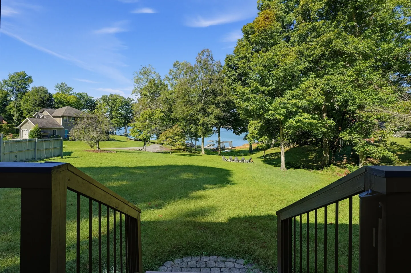 View looking down from deck railings toward a large grassy backyard leading to trees and a body of water.