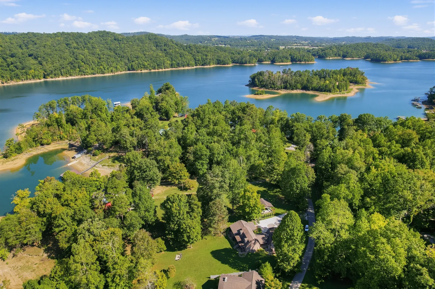 Aerial view of a lakefront residential property surrounded by dense green forest and a large blue lake with islands.