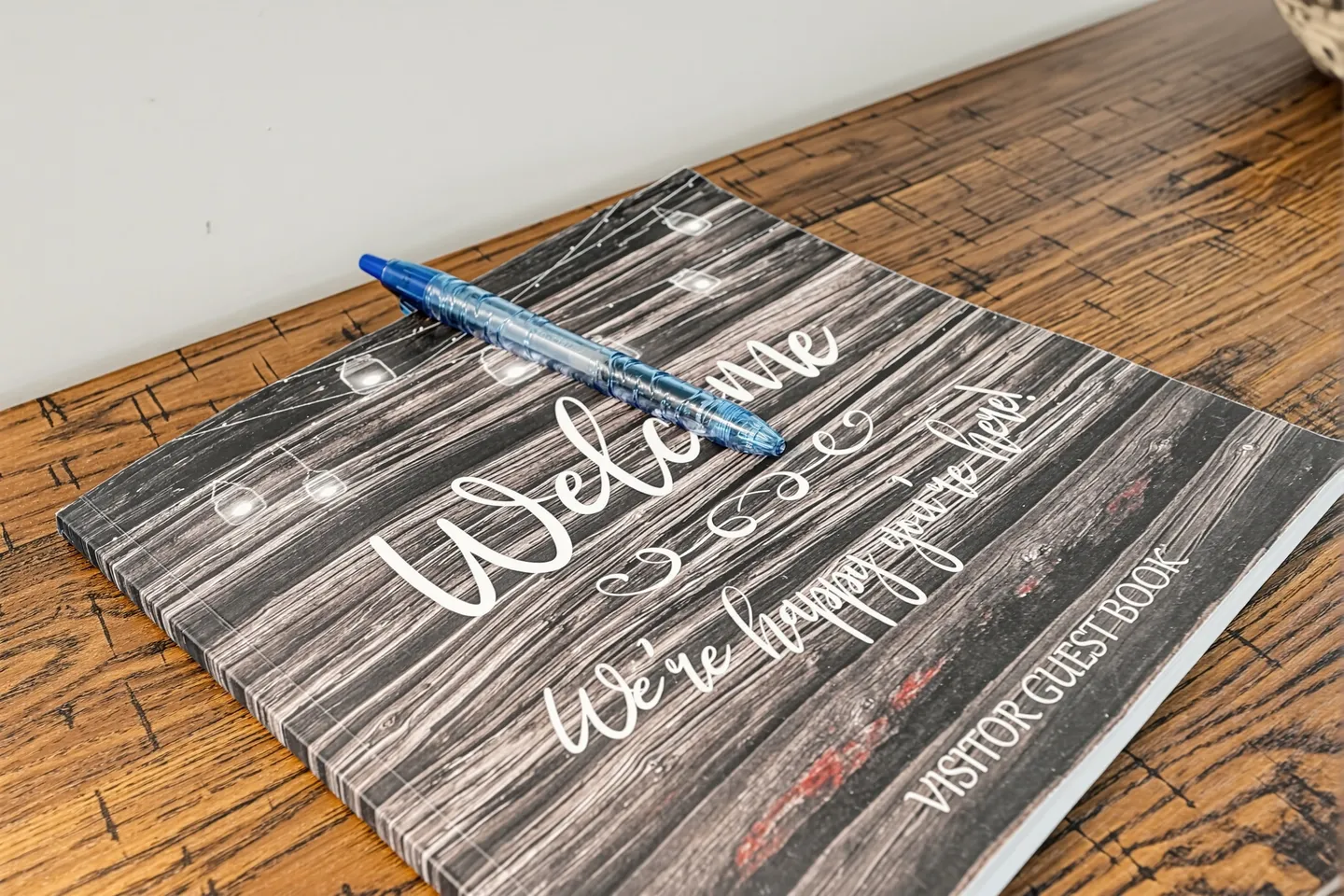 A guest welcome book with a wood-look cover and a blue pen resting on top, placed on a wooden surface.