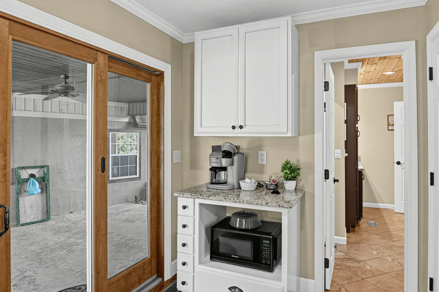 A dedicated coffee station with white cabinetry, microwave, and single-serve brewer next to a sliding glass door.
