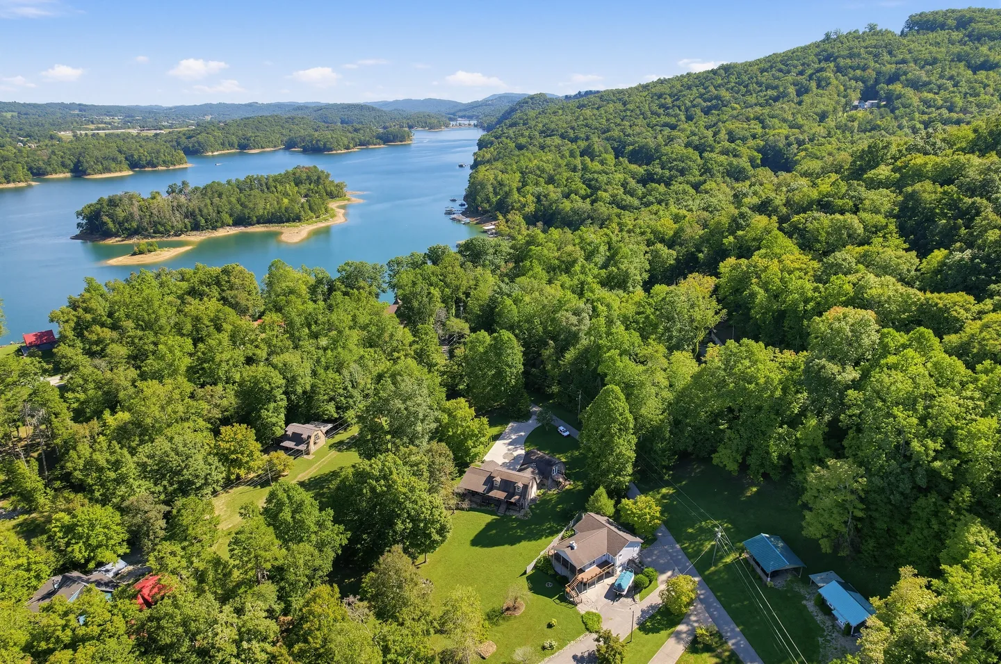 Aerial view of houses nestled among lush green trees near a large blue lake and rolling forested hills.