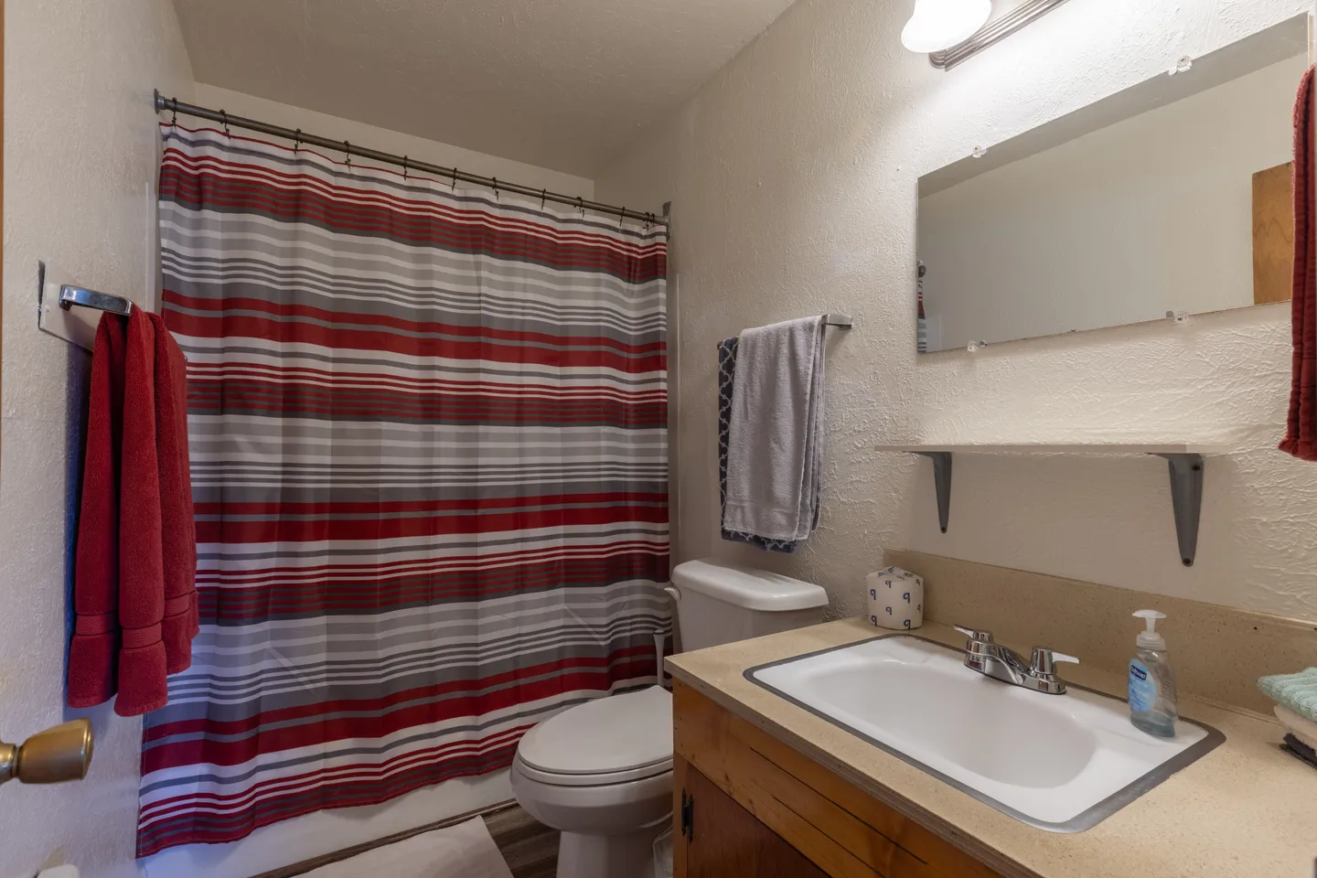 Bathroom featuring a vanity with a drop-in sink, a toilet, and a bathtub shower with a red, white, and grey striped shower curtain.