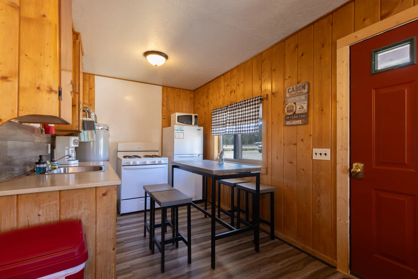 Kitchenette with wood paneled walls, a small gas stove, refrigerator, sink, and high-top dining table with stools.