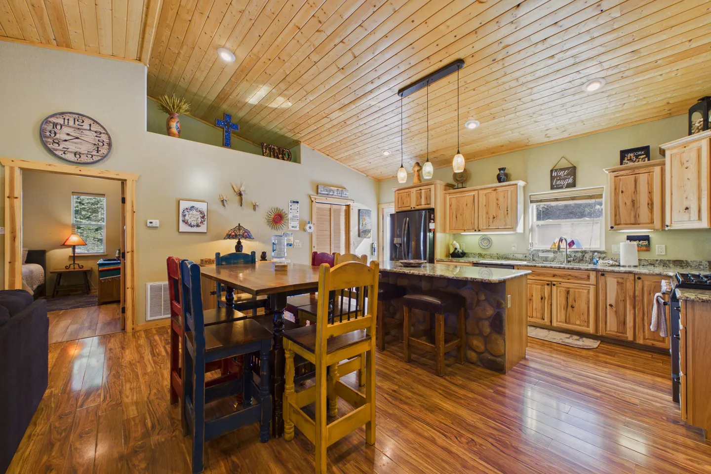 Open-concept kitchen and dining area featuring a wood-paneled angled ceiling, wood flooring, kitchen island, and colorful dining chairs.