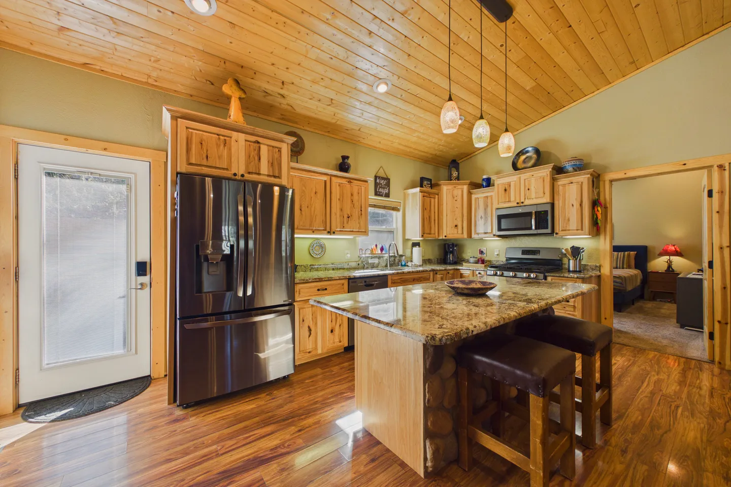 Kitchen with natural wood cabinets, wood-paneled ceiling, kitchen island with counter seating, and stainless steel appliances.