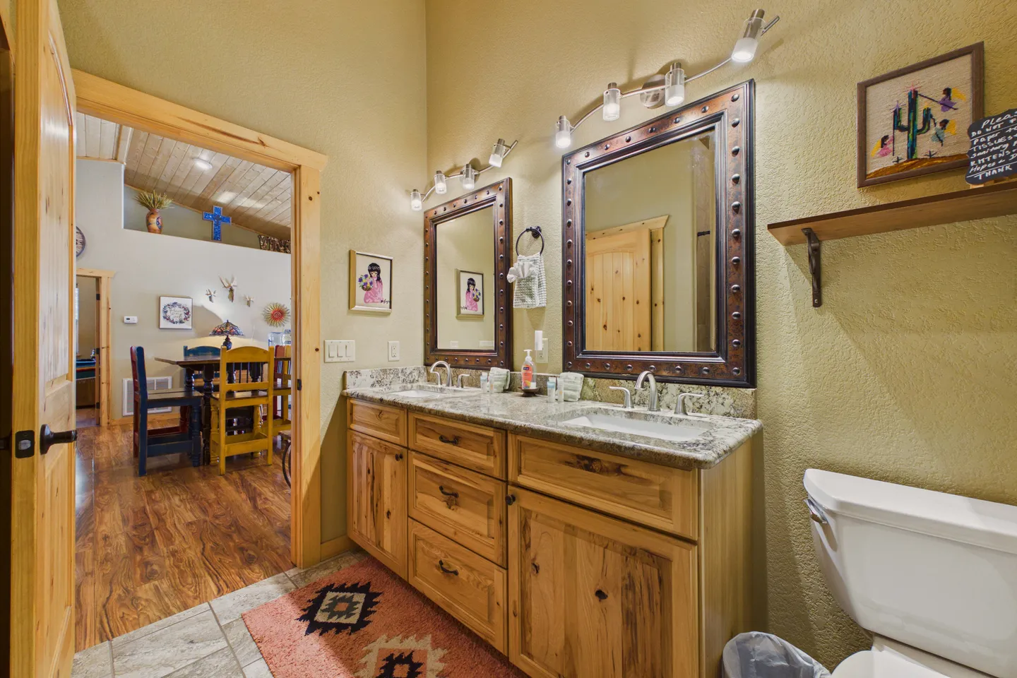 Bathroom featuring a double vanity with wooden cabinets, stone countertop, two framed mirrors, and a view into the dining area.