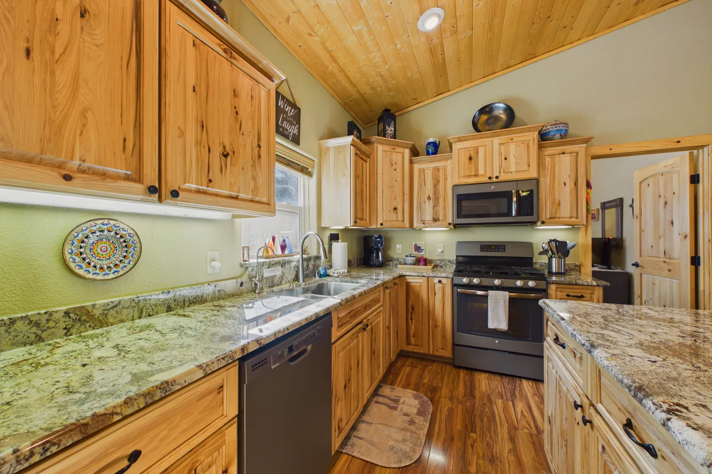 Kitchen with natural wood cabinets, granite countertops, and dark appliances beneath a wood-paneled ceiling.