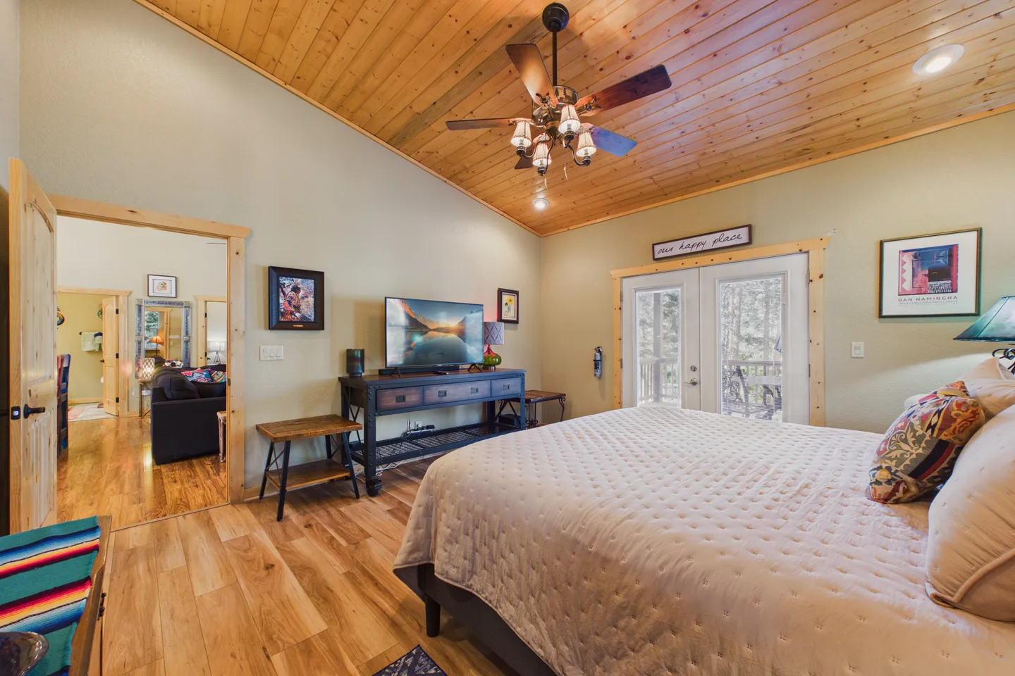 Bedroom with vaulted wood ceiling, ceiling fan, made bed, flat-screen television, and glass French doors leading outside.