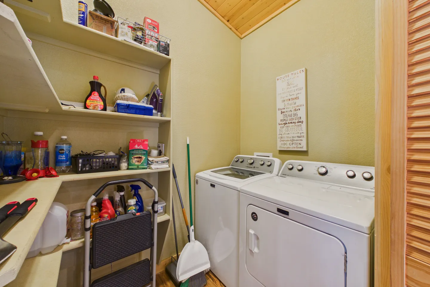Laundry room with a white washer and dryer next to built-in pantry shelves stocked with supplies.