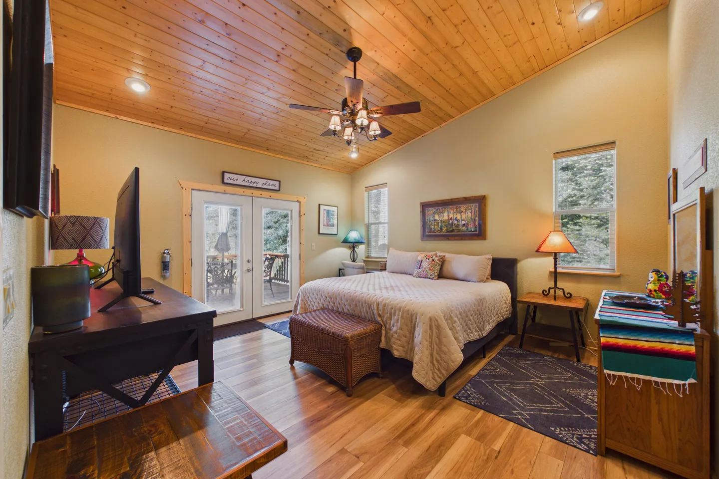 Bedroom with vaulted wood-paneled ceiling, ceiling fan, double bed, television on a stand, and glass French doors leading outside.