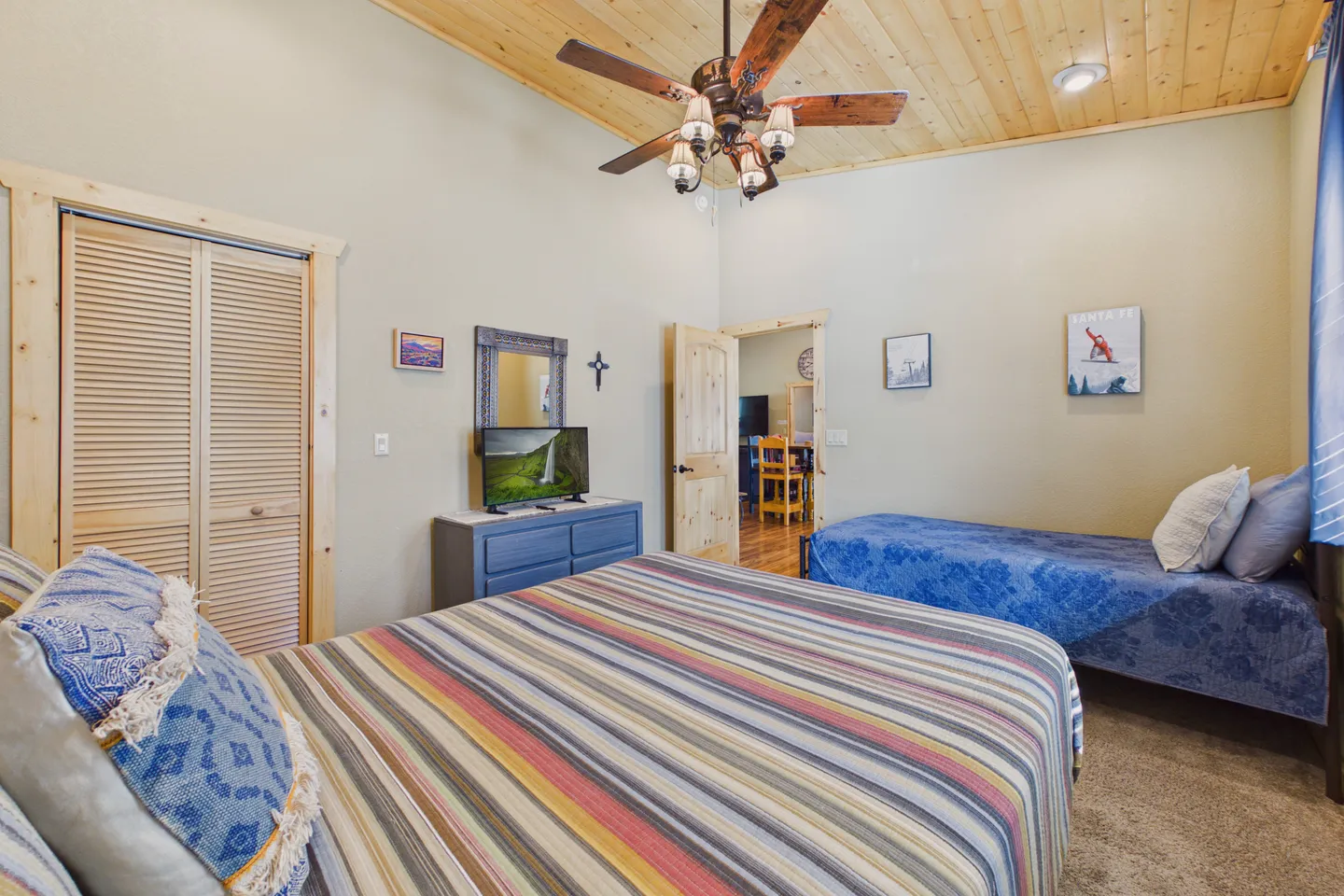 Bedroom featuring wood-paneled ceiling with ceiling fan, a striped bed in the foreground, and a blue daybed against the wall.