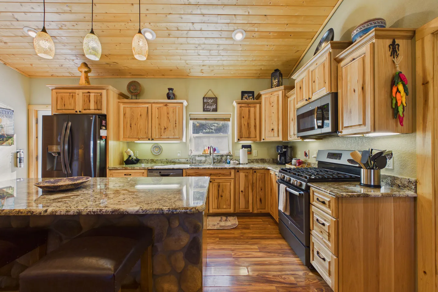 Kitchen with knotty wood cabinets, stone-look countertops, an island with stone base, dark appliances, and a wood plank ceiling.