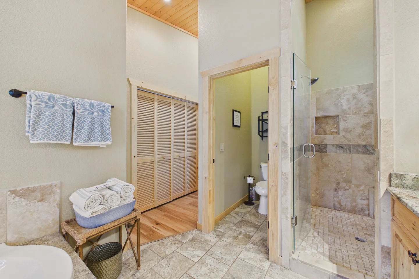 Bathroom with tile floors, a glass-door walk-in shower, an open water closet, and a hallway with louvered doors.