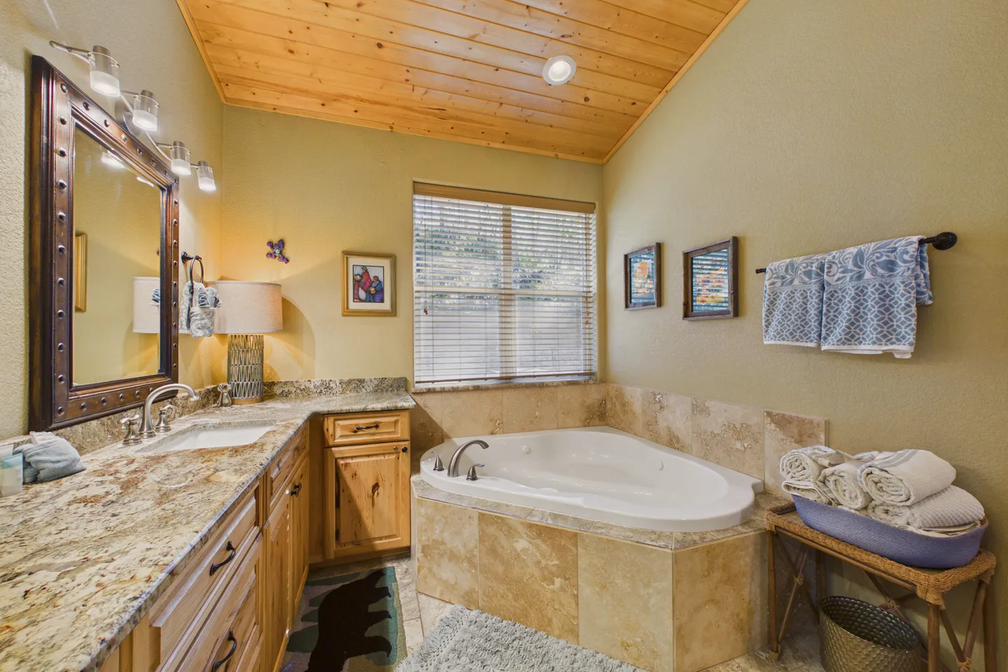Bathroom featuring a corner soaking tub with tile surround, wood cabinetry, granite countertop, and a wood-plank ceiling.